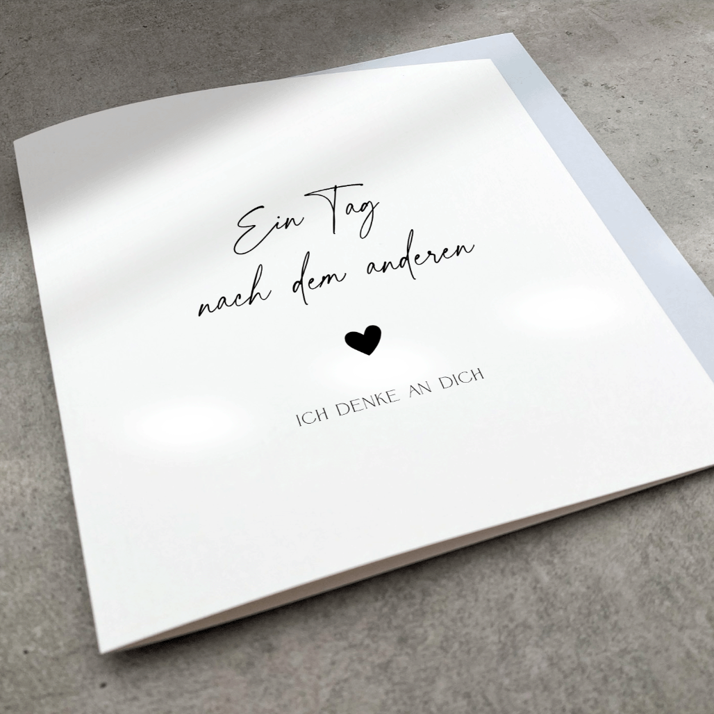 Minimalistische Trauerkarte mit schwarzem Text "Ein Tag nach dem anderen ♥ ich denke an Dich" mit schwarzem Herz und blaugrauem Umschlag