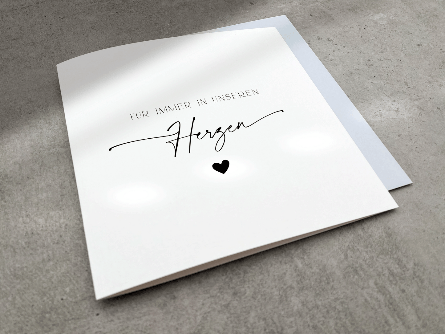 Weiße Trauerkarte mit schwarzem Text "Für immer in unseren Herzen" mit schwarzem Herz und Umschlag