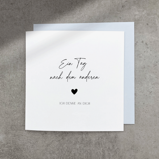 Quadratische Klappkarte mit schwarzem Text "Ein Tag nach dem anderen ♥ ich denke an Dich" mit blaugrauem Umschlag