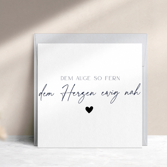 Quadratische Trauerkarte mit schwarzem Text "Dem Auge so fern, dem Herzen ewig nah" mit schwarzem Herz und blaugrauem Umschlag