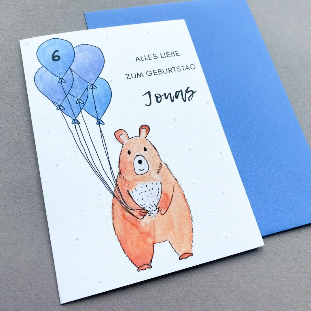 Glückwunschkarte zum Geburtstag mit Bär der blaue Luftballons hält und blauem Umschlag
