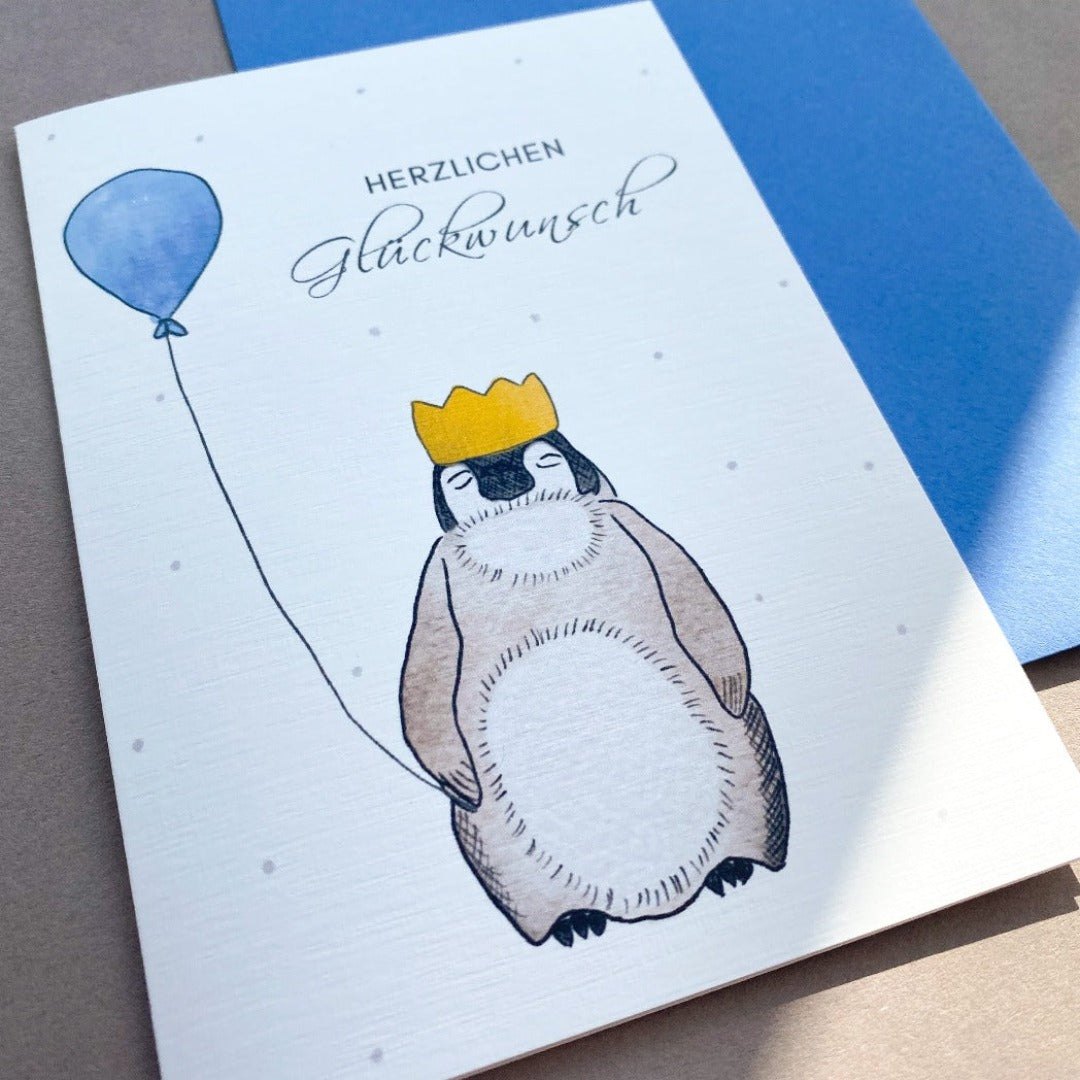 Geburtstagskarte mit gezeichnetem Pinguin und blauen Luftballons und blauem Umschlag