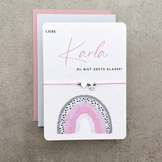 Karte zur Einschulung mit gezeichnetem Regenbogen und Armband in silber, mit rosa oder grauem Umschlag